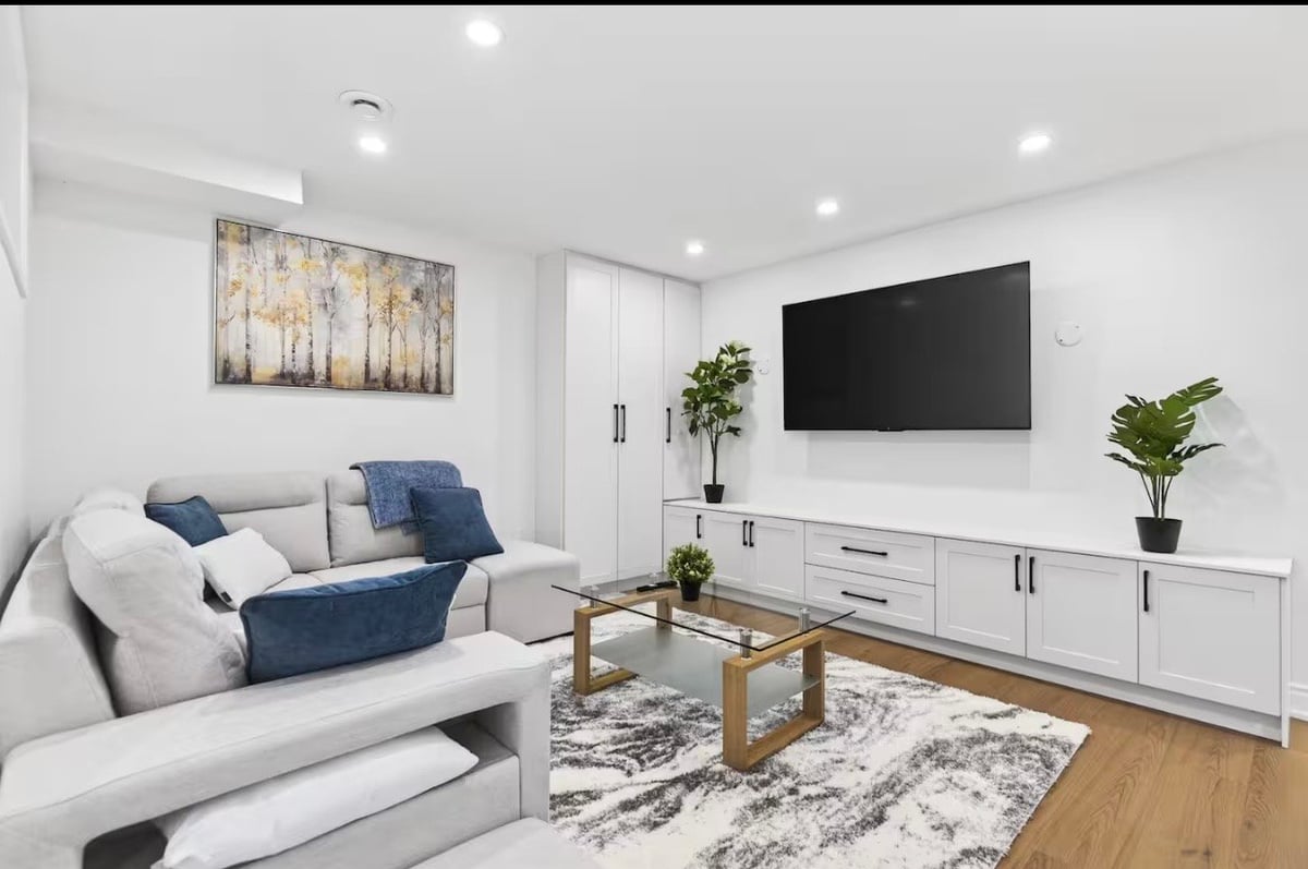 Modern living room with white sectional sofa, mounted TV, white media cabinet, and wooden coffee table on area rug